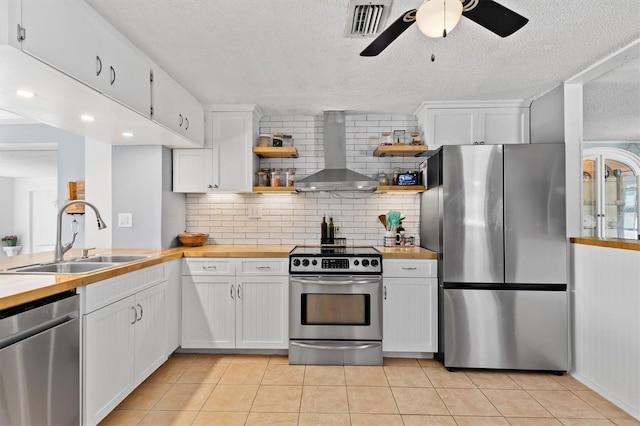 kitchen with wall chimney range hood, appliances with stainless steel finishes, a sink, and butcher block counters