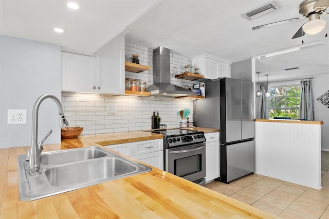 kitchen featuring butcher block countertops, a sink, white cabinets, appliances with stainless steel finishes, and wall chimney exhaust hood