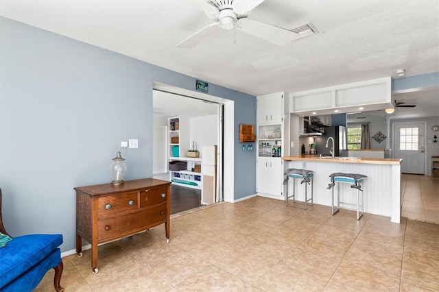 kitchen with a ceiling fan, a breakfast bar area, a peninsula, a textured ceiling, and white cabinetry