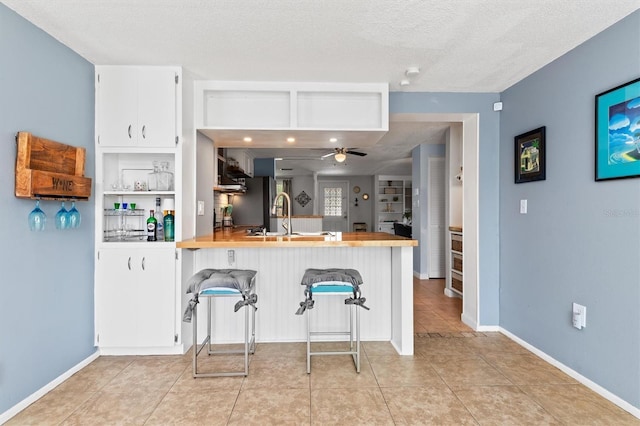 kitchen with a textured ceiling, ceiling fan, a breakfast bar area, a peninsula, and a sink