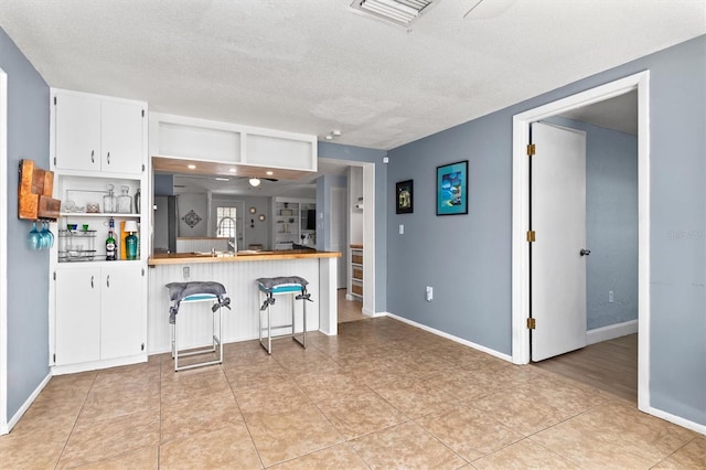 kitchen with a textured ceiling, visible vents, baseboards, white cabinets, and a kitchen bar