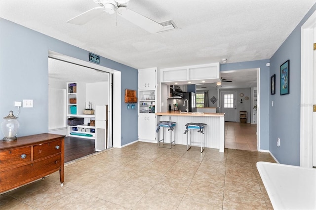 kitchen with light tile patterned floors, a peninsula, a breakfast bar, a sink, and a ceiling fan