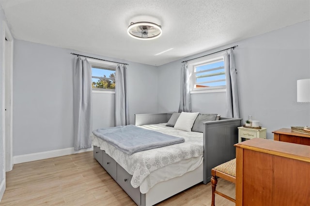 bedroom featuring baseboards, a textured ceiling, and light wood finished floors