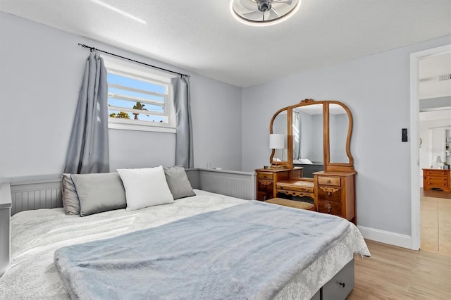 bedroom with a textured ceiling, light wood-type flooring, visible vents, and baseboards