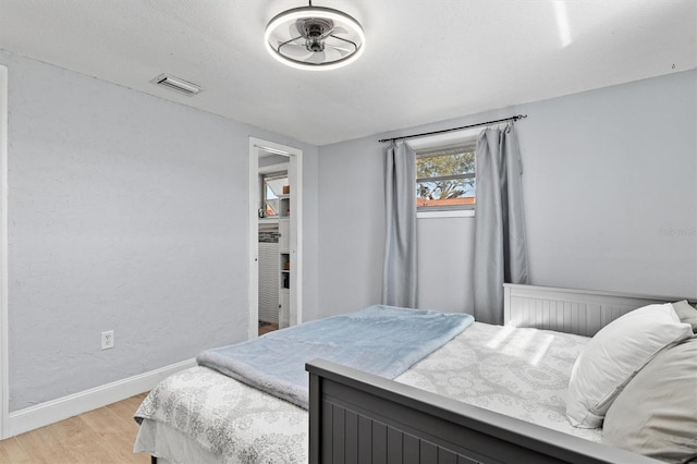 bedroom with a textured wall, light wood finished floors, visible vents, and baseboards