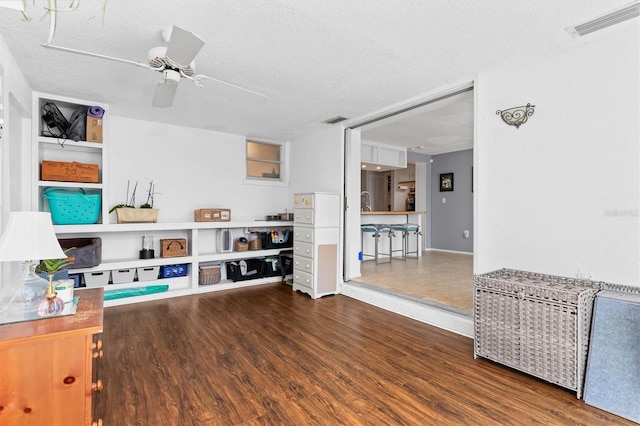 interior space featuring a ceiling fan, a textured ceiling, visible vents, and wood finished floors