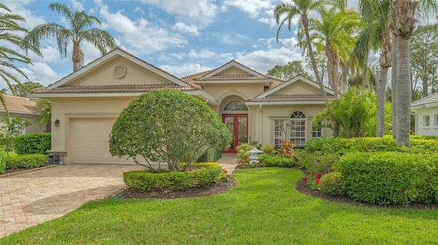 mediterranean / spanish-style house with a garage, a tiled roof, french doors, decorative driveway, and stucco siding