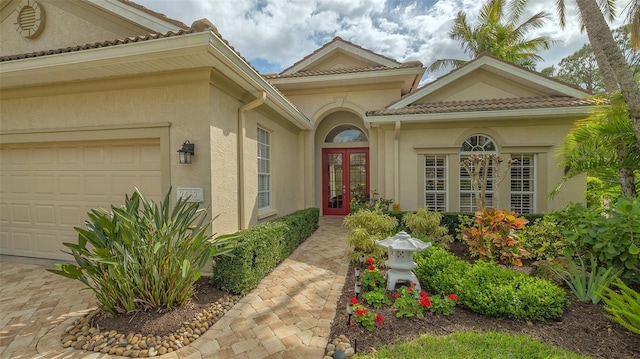 entrance to property with a garage, french doors, a tiled roof, and stucco siding