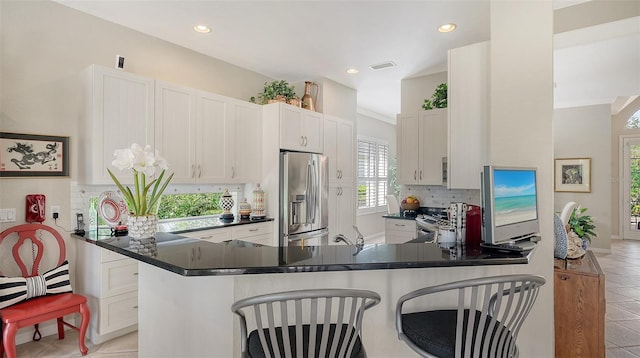 kitchen featuring stainless steel appliances, white cabinets, a kitchen breakfast bar, decorative backsplash, and dark countertops