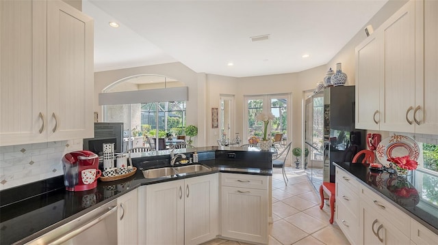 kitchen featuring dark countertops, a peninsula, a sink, backsplash, and light tile patterned flooring