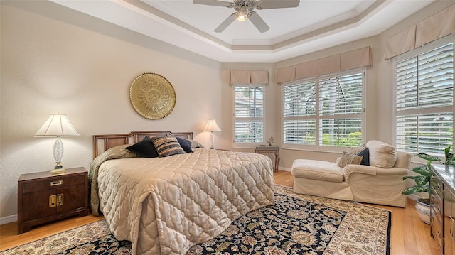 bedroom with light wood-style floors, a tray ceiling, crown molding, and baseboards