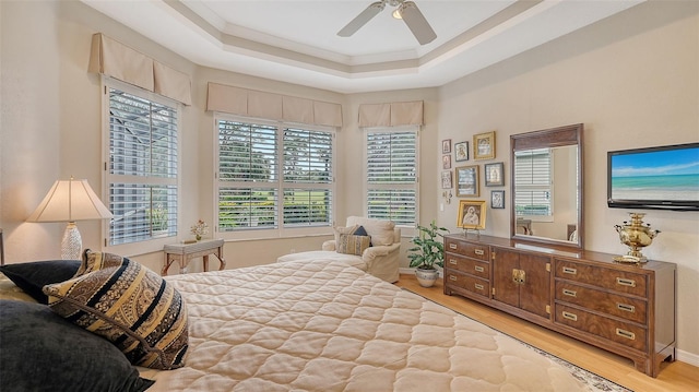 bedroom featuring a ceiling fan, a tray ceiling, crown molding, and wood finished floors