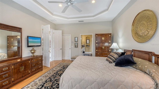 bedroom with light wood-type flooring, a raised ceiling, visible vents, and crown molding