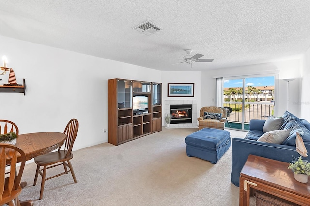 living room with a fireplace, visible vents, a ceiling fan, light carpet, and a textured ceiling