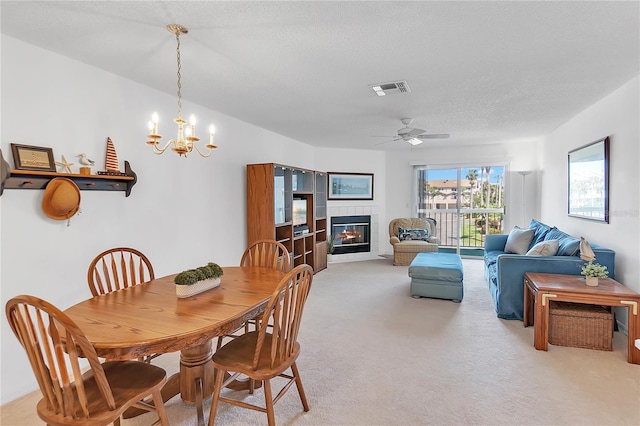 dining area with visible vents, light colored carpet, a textured ceiling, a fireplace, and ceiling fan with notable chandelier