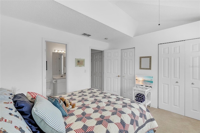 bedroom featuring light carpet, a textured ceiling, two closets, and visible vents