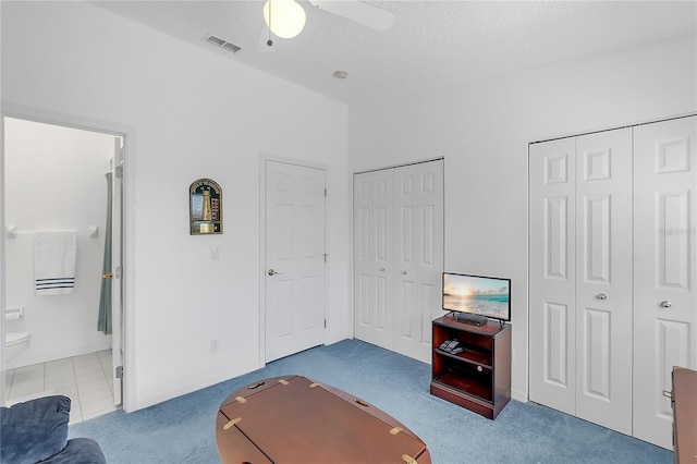 carpeted bedroom featuring visible vents, a ceiling fan, connected bathroom, a textured ceiling, and multiple closets