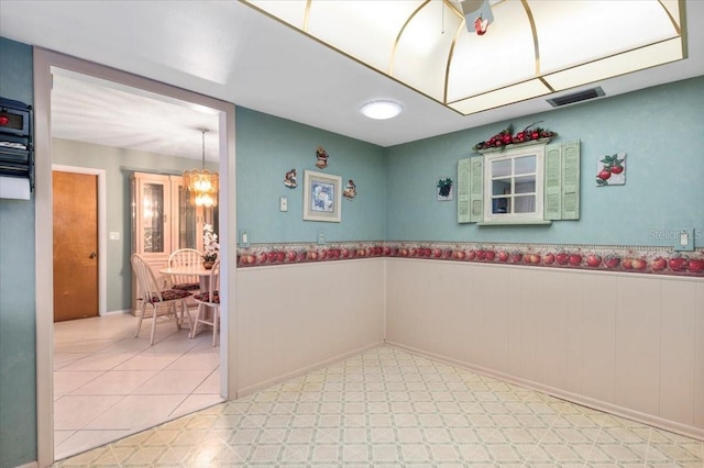 empty room featuring light floors, visible vents, a chandelier, and wainscoting