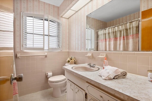 full bath featuring toilet, a wainscoted wall, tile walls, vanity, and wallpapered walls