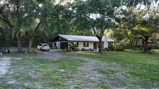 view of front of home with a garage, a front lawn, a chimney, and dirt driveway