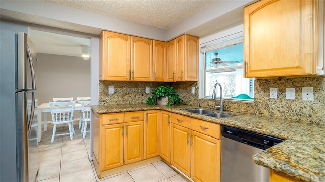 kitchen with light tile patterned floors, ceiling fan, stainless steel appliances, a sink, and light stone countertops