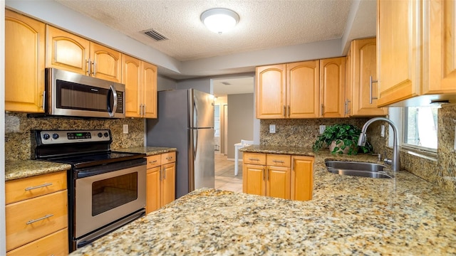 kitchen with visible vents, light stone countertops, stainless steel appliances, tasteful backsplash, and a sink