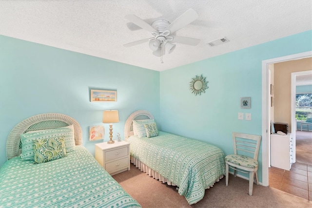 carpeted bedroom featuring a textured ceiling, ceiling fan, tile patterned flooring, and visible vents