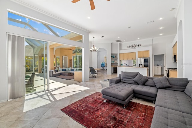 living area with ceiling fan with notable chandelier, ornamental molding, arched walkways, and recessed lighting