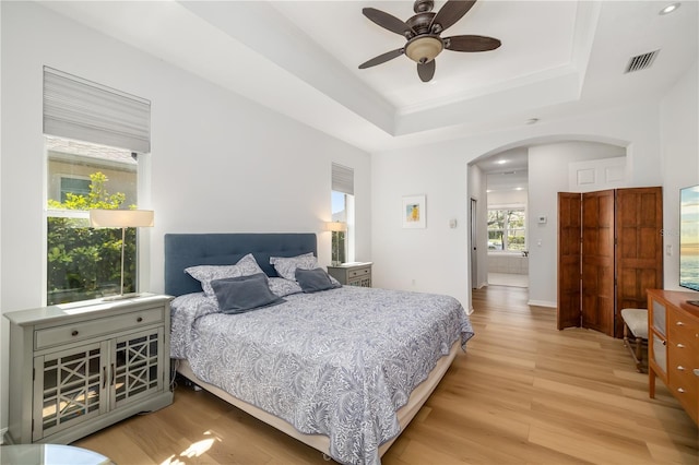 bedroom with light wood-type flooring, arched walkways, and a tray ceiling