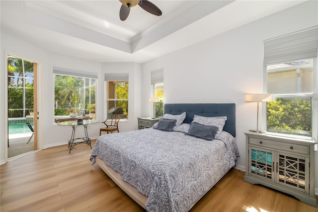 bedroom featuring access to outside, a raised ceiling, multiple windows, and wood finished floors