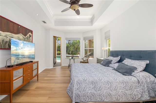 bedroom with visible vents, baseboards, light wood-style flooring, ornamental molding, and a tray ceiling