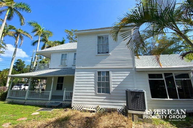 back of property with a balcony, roof with shingles, cooling unit, a yard, and a porch