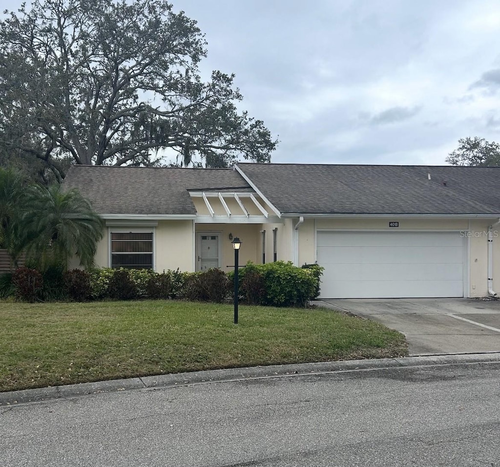 view of front of house with roof with shingles, stucco siding, a garage, driveway, and a front lawn