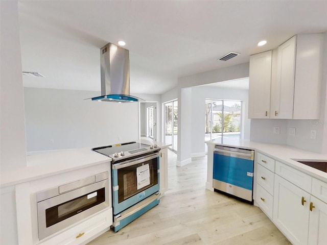 kitchen with island range hood, visible vents, white cabinets, light wood-style floors, and appliances with stainless steel finishes