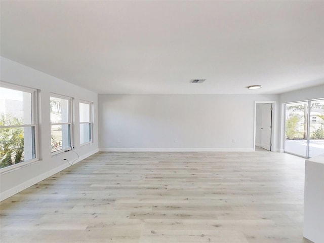 empty room with light wood-type flooring, visible vents, and baseboards