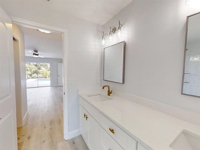 bathroom featuring wood finished floors, a sink, a ceiling fan, baseboards, and double vanity