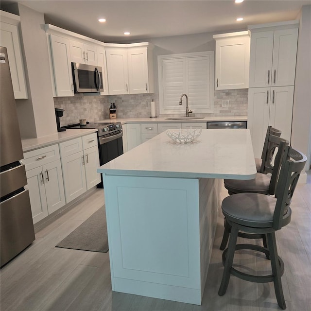 kitchen featuring a breakfast bar, a sink, light wood-style floors, appliances with stainless steel finishes, and a center island