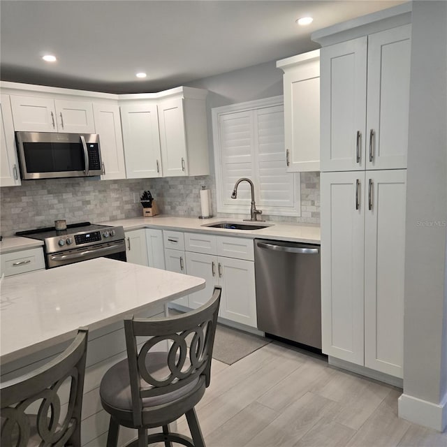 kitchen featuring tasteful backsplash, light countertops, appliances with stainless steel finishes, white cabinetry, and a sink