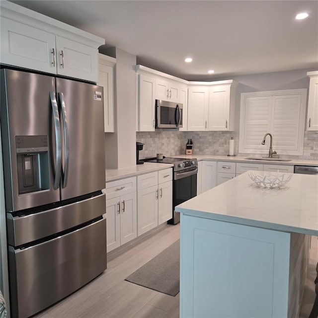 kitchen featuring a sink, light wood-style floors, appliances with stainless steel finishes, white cabinets, and decorative backsplash