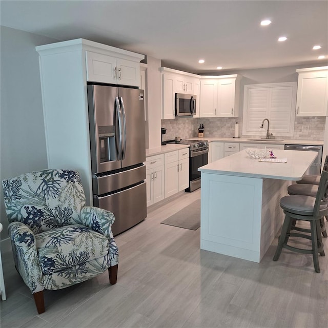 kitchen with a sink, stainless steel appliances, light countertops, white cabinetry, and tasteful backsplash