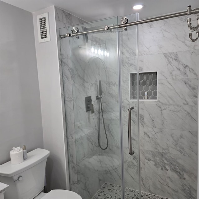 bathroom with a marble finish shower, visible vents, and toilet