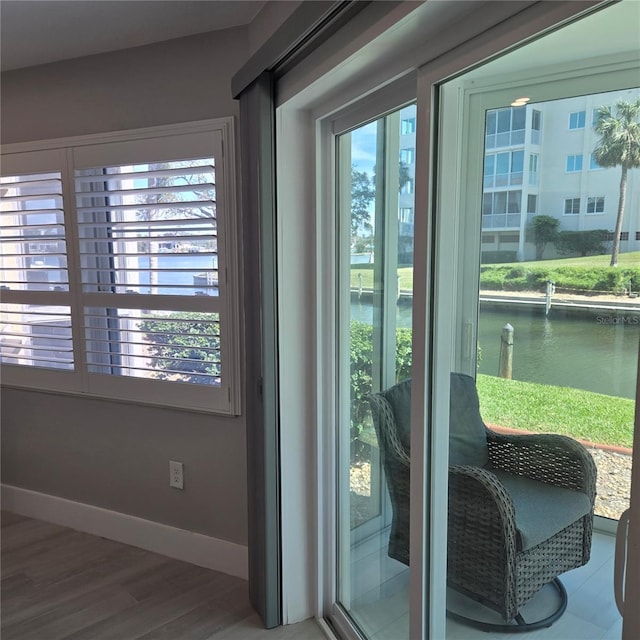 doorway with baseboards, a water view, and wood finished floors
