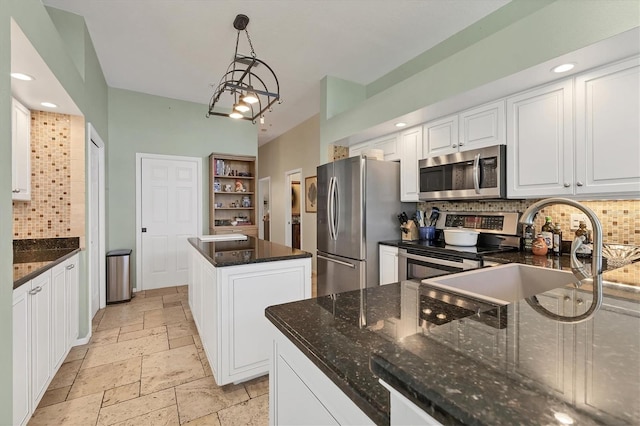 kitchen with stone tile floors, stainless steel appliances, white cabinetry, backsplash, and dark stone countertops