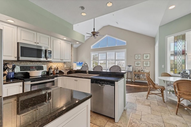 kitchen with stone tile flooring, backsplash, appliances with stainless steel finishes, white cabinets, and a sink