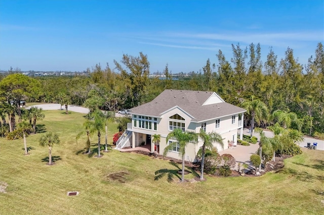 rear view of property featuring driveway, a lawn, and stairs