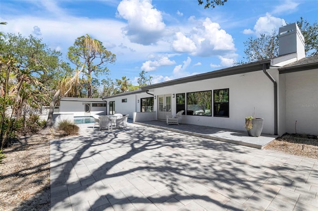 back of property featuring french doors, a patio area, a chimney, and stucco siding