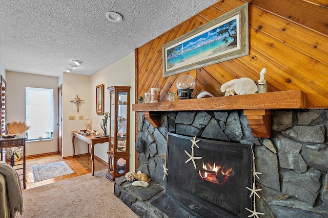 living area with carpet floors, a stone fireplace, wooden walls, and a textured ceiling