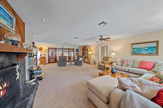 carpeted living room featuring a ceiling fan, visible vents, a stone fireplace, and a textured ceiling