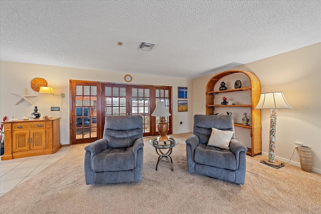 living area with a textured ceiling, tile patterned flooring, carpet floors, visible vents, and french doors