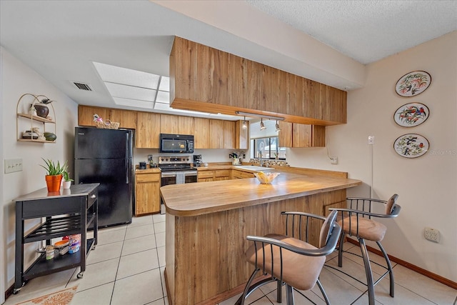 kitchen with light tile patterned floors, a breakfast bar area, a peninsula, visible vents, and black appliances